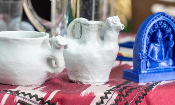 Trzy modele 3D przedstawiające artefakty ustawione na tkaninie z etnicznym wzorem.