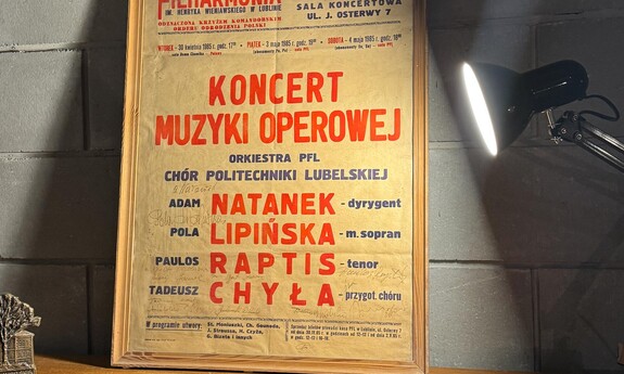 Plakat koncertu muzyki operowej z lat 60., wystawiony w ramce i oświetlony lampką. Plakat zapowiada występ w Państwowej Filharmonii im. H. Wieniawskiego w Lublinie przy ul. J. Osterwy 7. 